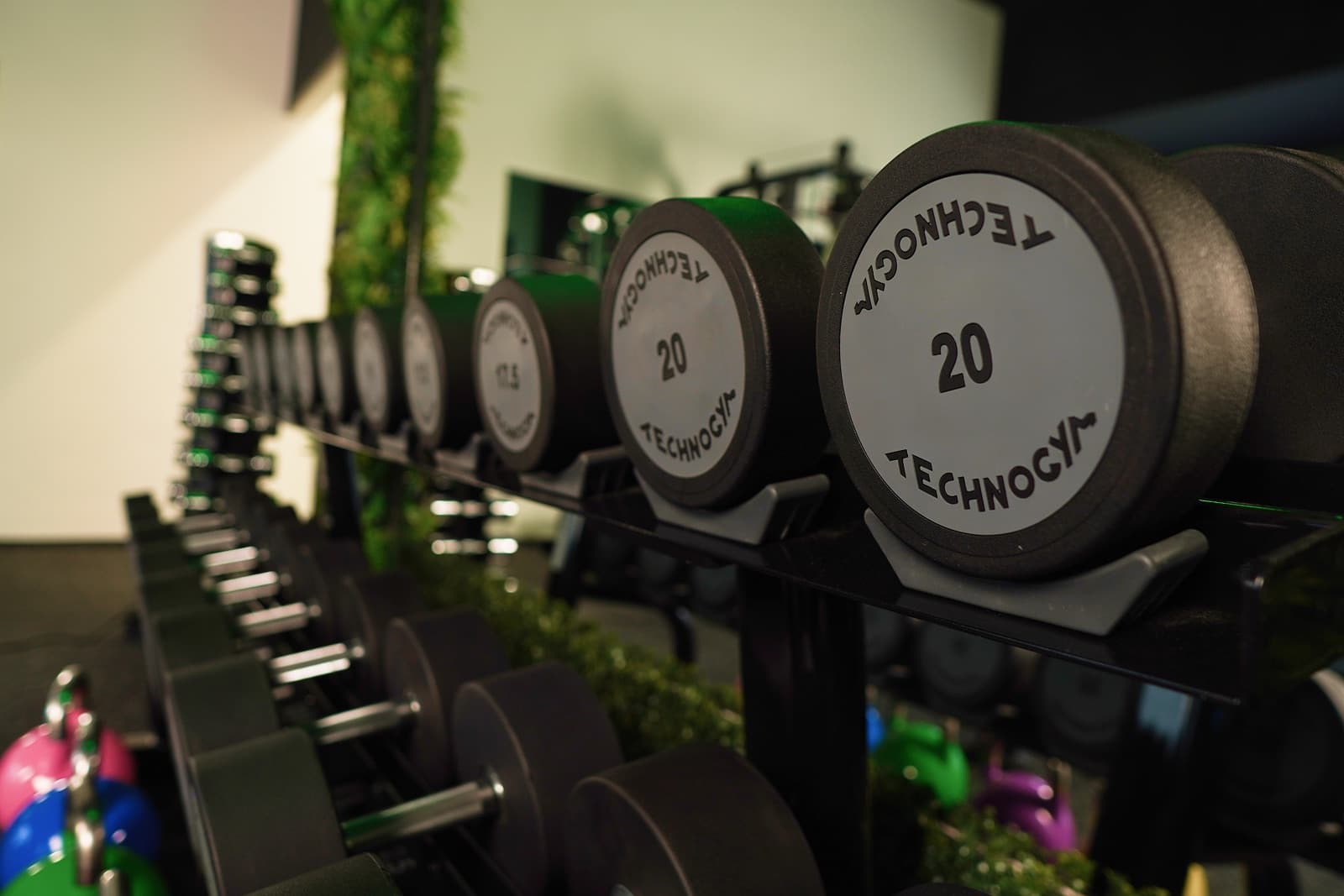 Detail řady jednoruček Technogym srovnaných na stojanu v posilovně The Jungle